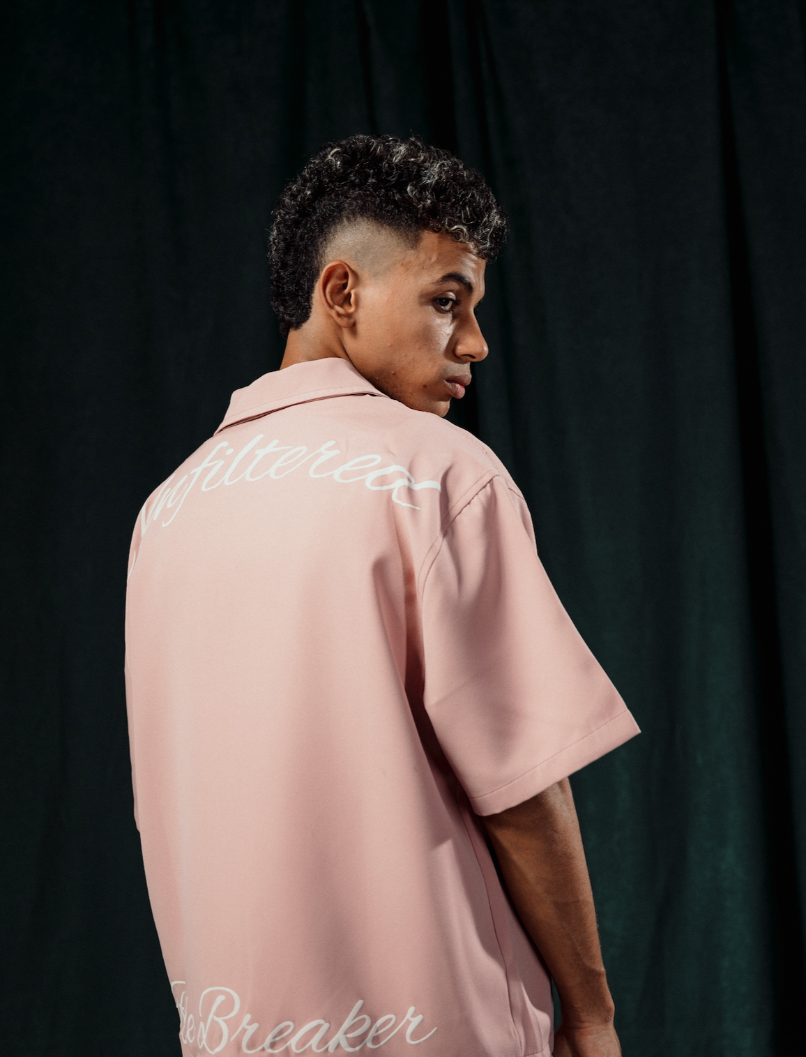 Person wearing a pink shirt with text on the back against a dark background